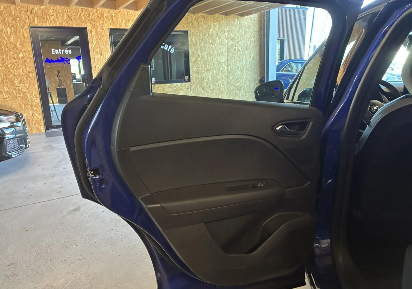 Vue rapprochée de la porte arrière gauche ouverte d’un Renault Captur bleu, intérieur noir avec poignée et commande de vitre.