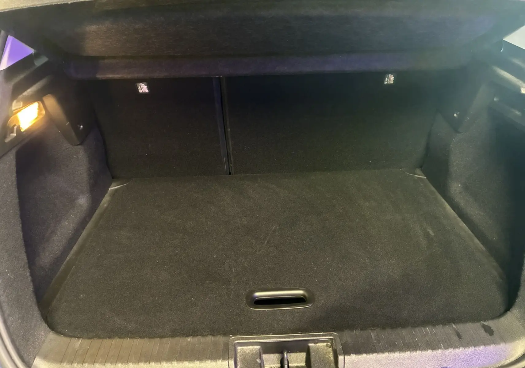 Coffre vide vu de l'arrière d'un Renault Captur bleu 1.3 TCE 140 Intens, revêtement noir et éclairage latéral allumé.