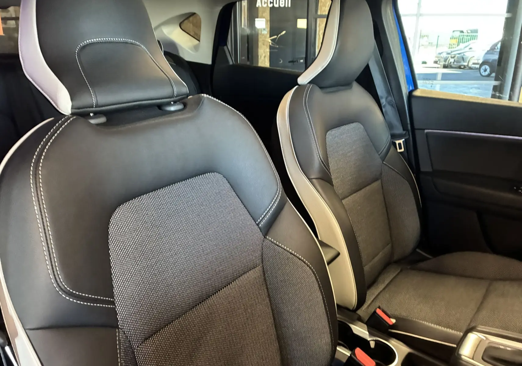 Vue intérieure rapprochée des sièges avant en tissu noir avec surpiqûres blanches du Renault Captur bleu 2021.