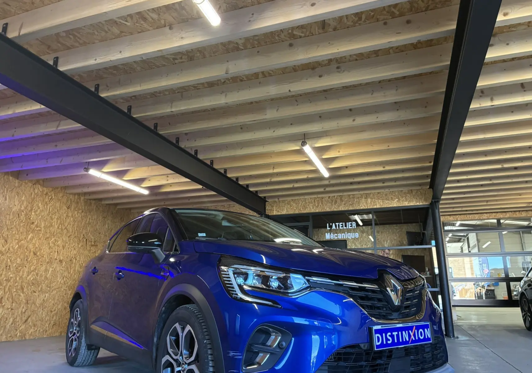 Renault Captur 1.3 TCE 140 Intens bleu en 3/4 avant droit, avec calandre noire et phares LED, stationné en intérieur bois.