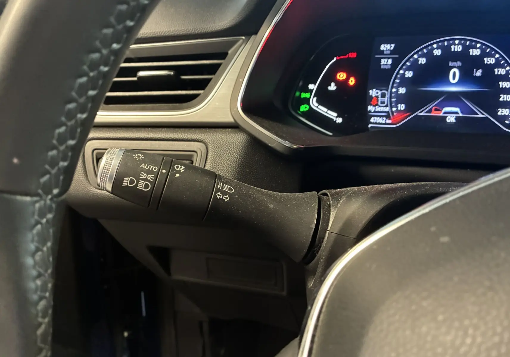 Vue intérieure rapprochée du commodo d’éclairage à gauche du volant du Renault Captur bleu, avec tableau de bord numérique en arrière-plan.