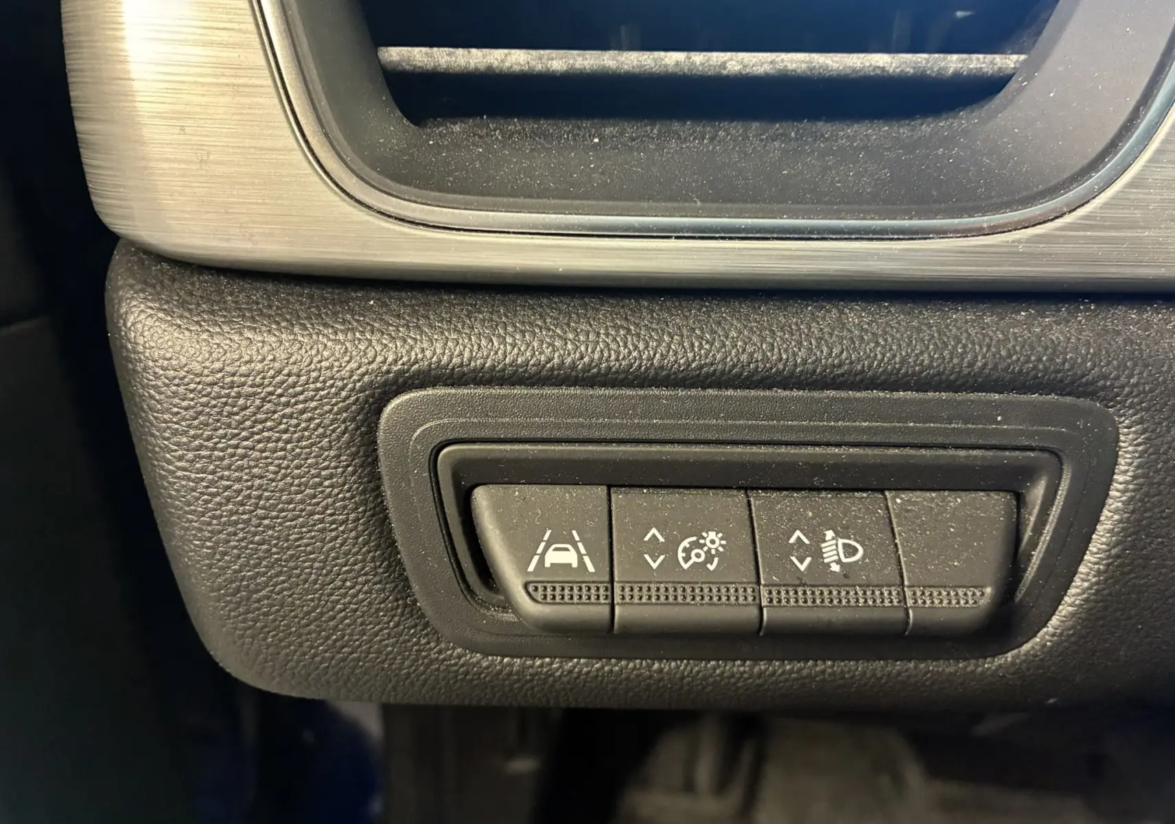 Gros plan sur les commandes d'assistance à la conduite dans un Renault Captur bleu, boutons pour régulateur, phares et maintien de voie.