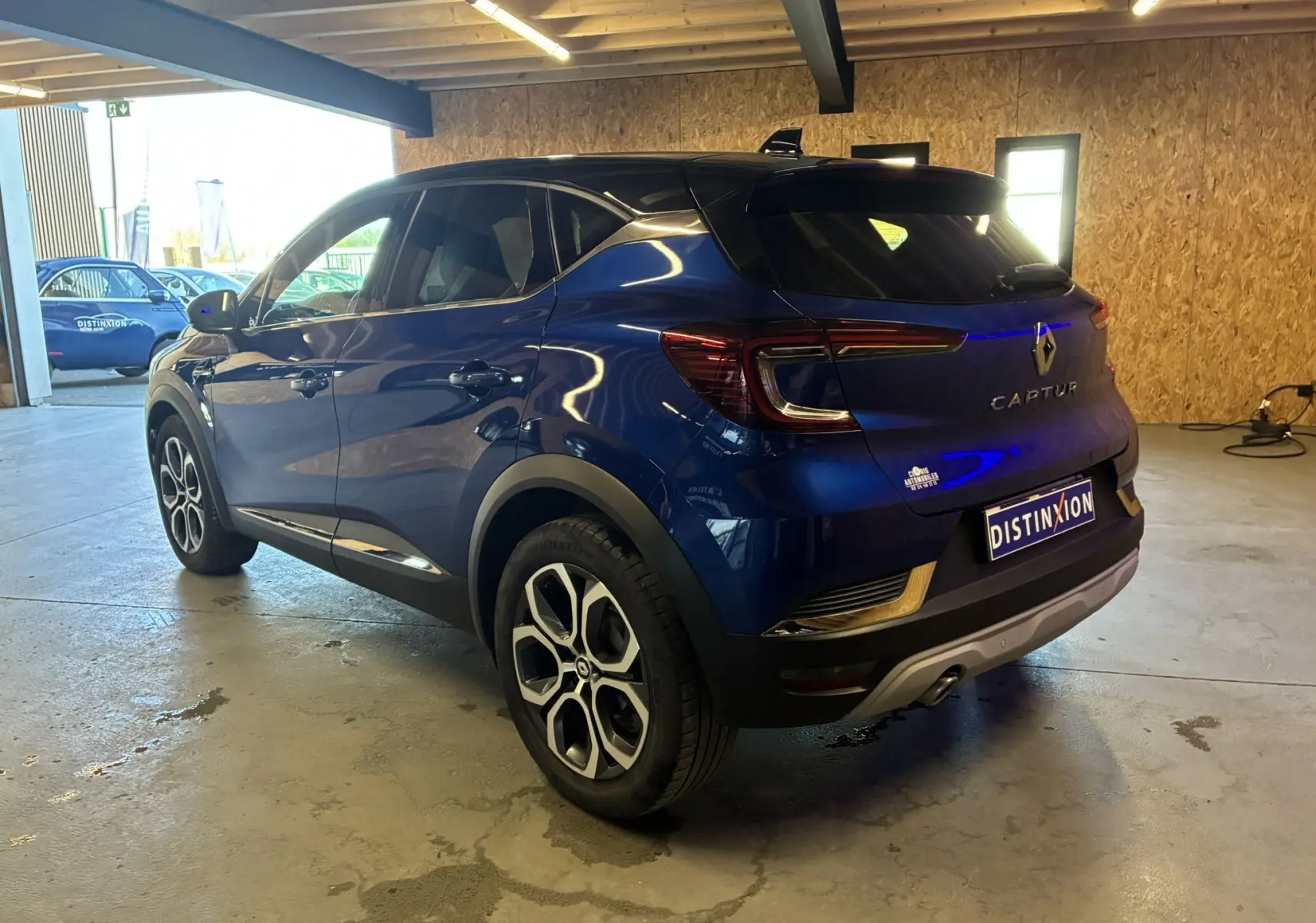 Vue 3/4 arrière droite d'un Renault Captur bleu 2021 avec toit noir et jantes distinctives en intérieur d'atelier.
