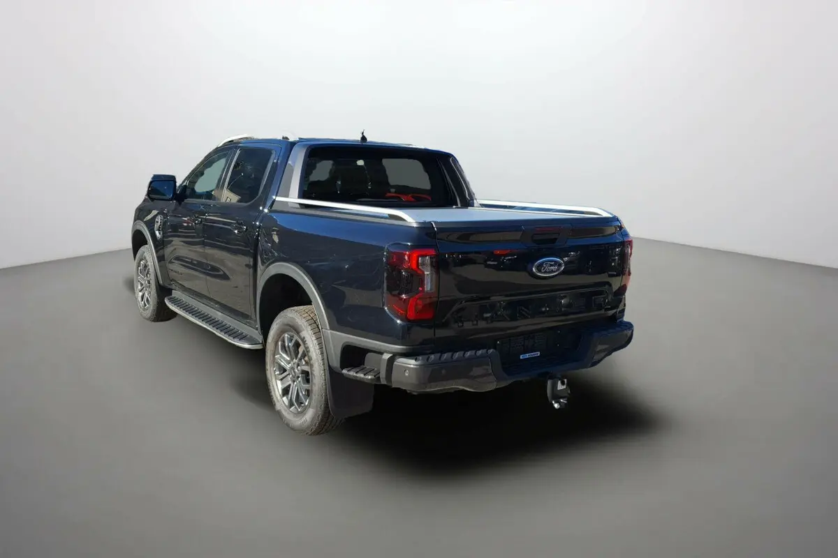 Ford Ranger noir agate en 3/4 arrière droit, double cabine avec attelage et barres de toit visibles.