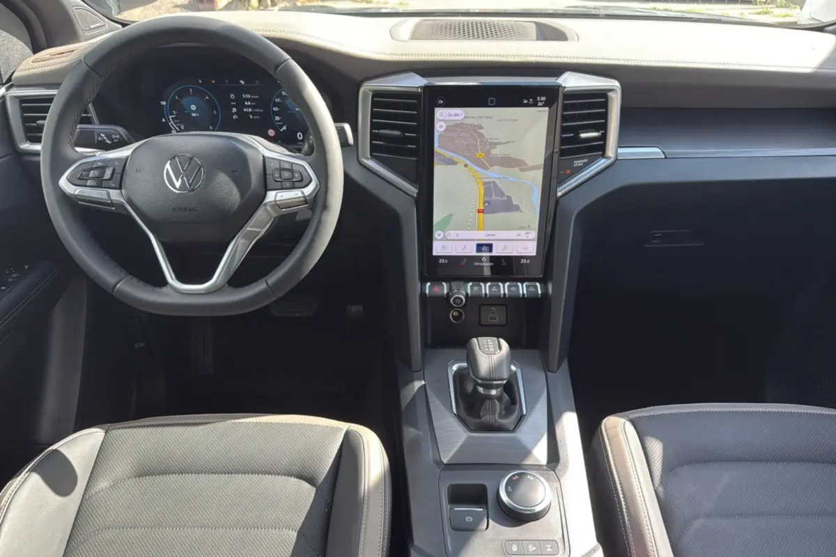 Vue intérieure avant du Volkswagen Amarok 2026 avec tableau de bord noir, écran tactile vertical et volant multifonctions cuir.