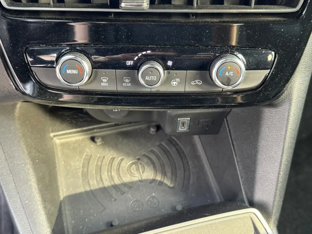 Gros plan sur la console centrale de l’Opel Mokka électrique 2025, montrant les commandes de climatisation et un espace de recharge sans fil.