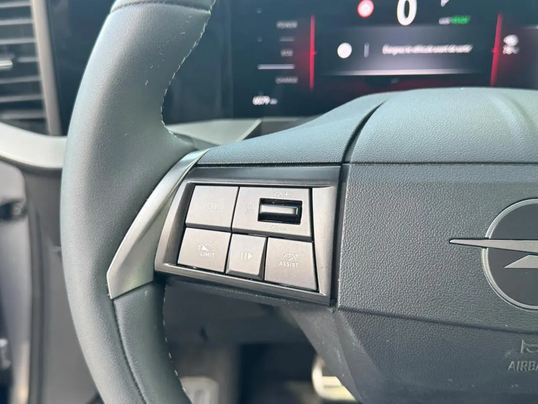 Gros plan sur le volant gris de l’Opel Mokka électrique 2025, avec commandes intégrées à gauche et logo Opel visible.
