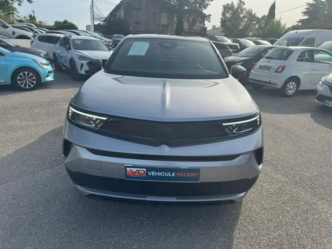 Vue avant d'un Opel Mokka électrique gris 2025 avec calandre noire et phares LED fins, stationné en extérieur.
