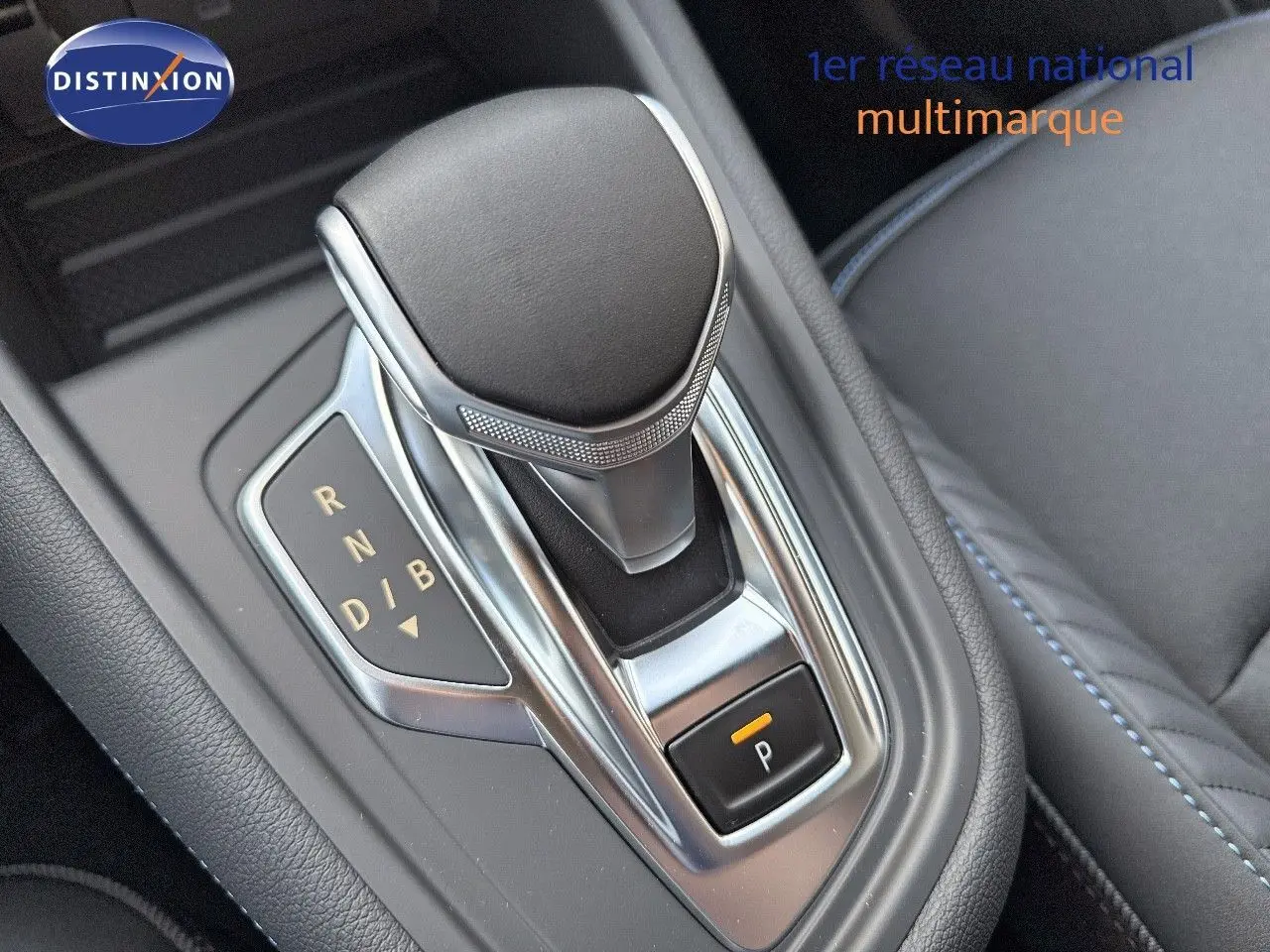 Le levier de vitesses automatique de la Renault Symbioz E-Tech 145 en gros plan, avec sellerie grise et surpiqûres bleues.