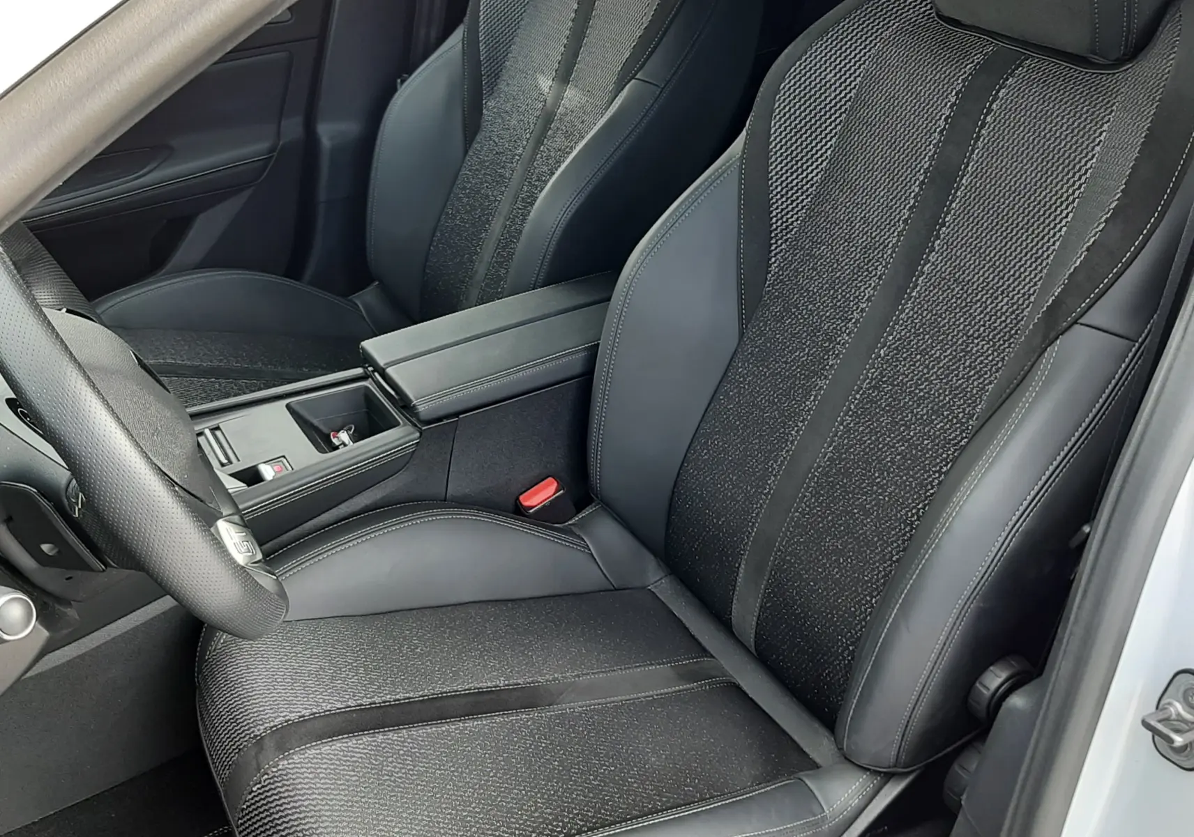 Vue intérieure côté conducteur de la Peugeot 308 SW 2024, sièges noirs avec logo Peugeot brodé sur l'appuie-tête.