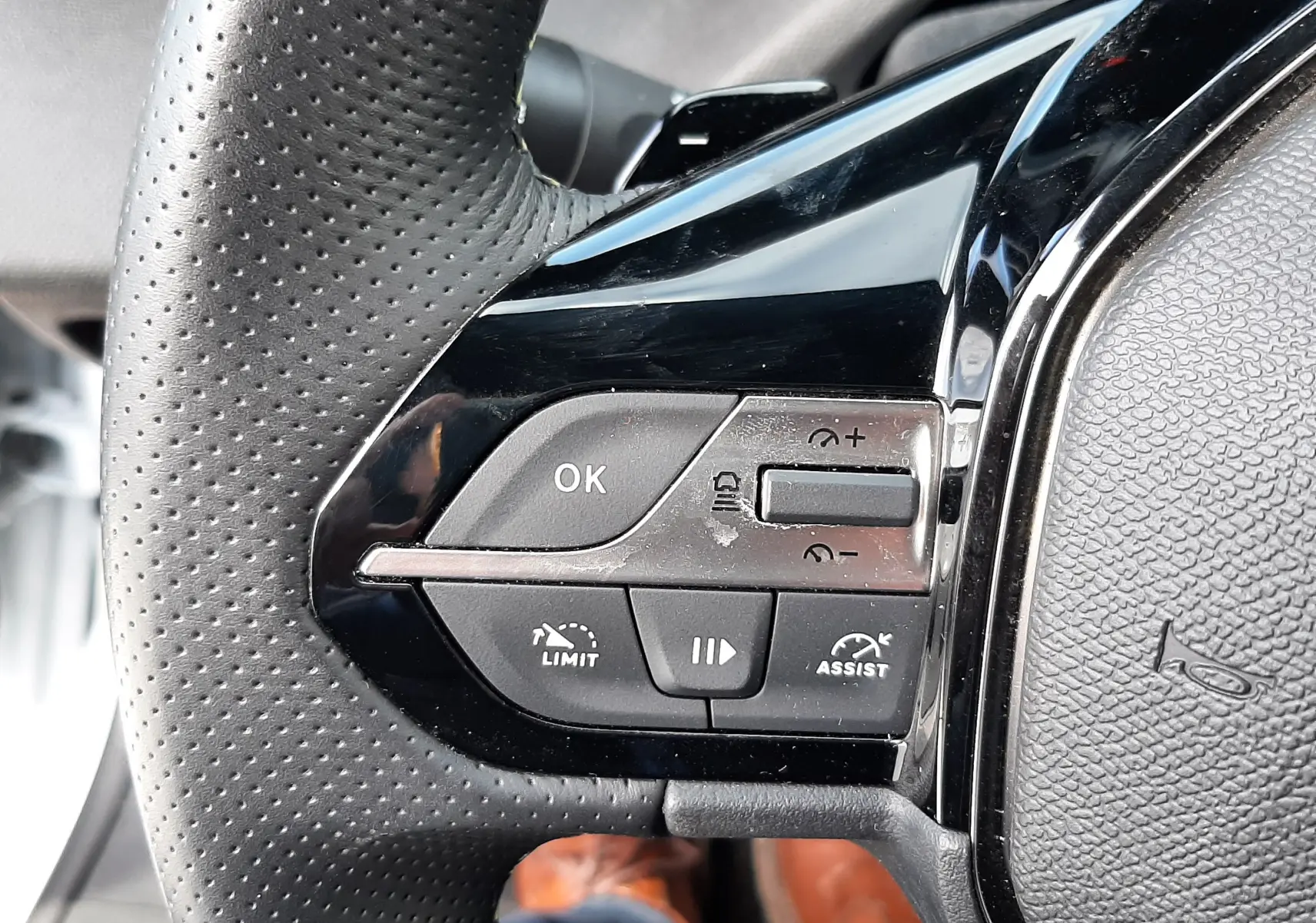 Gros plan sur les commandes à gauche du volant perforé noir du Peugeot 308 SW blanc Okenite, avec boutons de limitation et assistance.