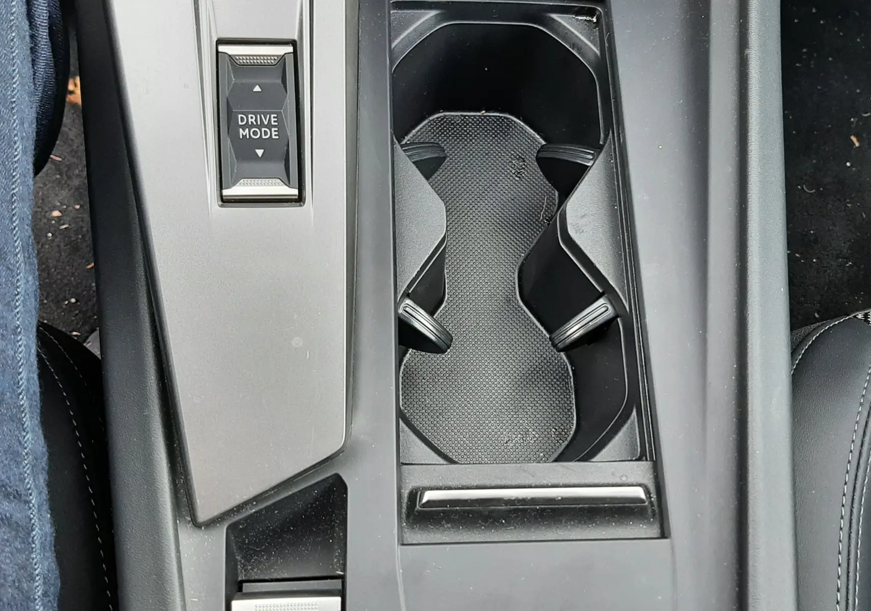 Vue plongeante sur la console centrale noire du Peugeot 308 SW 2024, avec porte-gobelets et bouton Drive Mode.