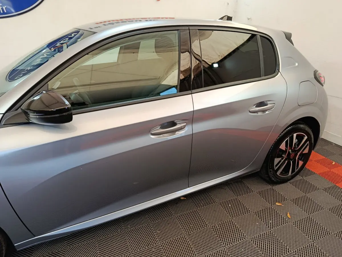 Profil côté gauche d'une Peugeot 208 gris clair 2025 avec jantes noires et rétroviseur noir brillant.