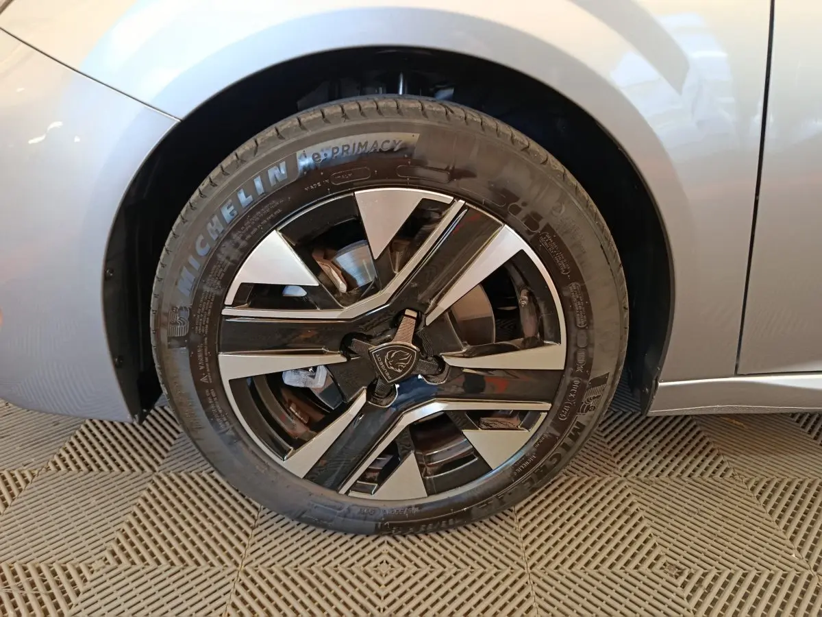 Gros plan sur la roue avant gauche gris clair d'une Peugeot 208 PureTech 100 S&S Allure avec jante noire et argentée.
