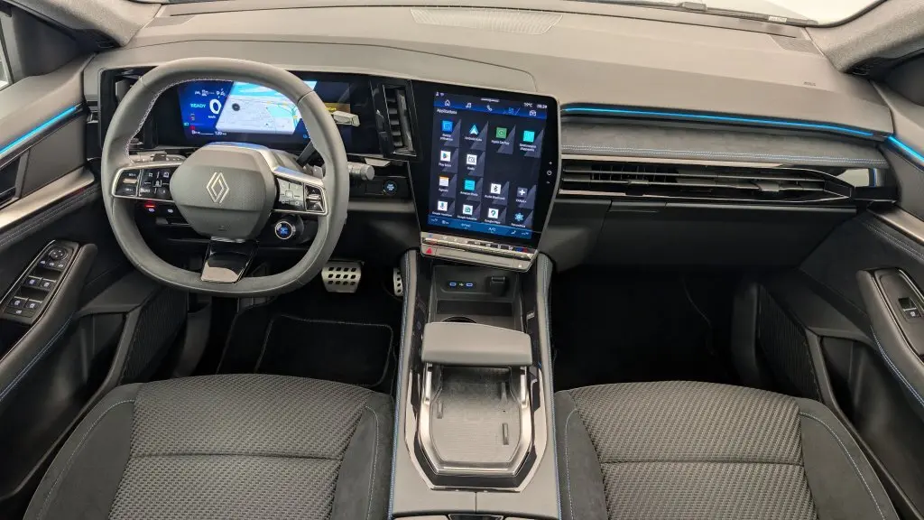 Vue intérieure avant du Renault Espace E-Tech gris avec tableau de bord numérique et écran tactile vertical lumineux.