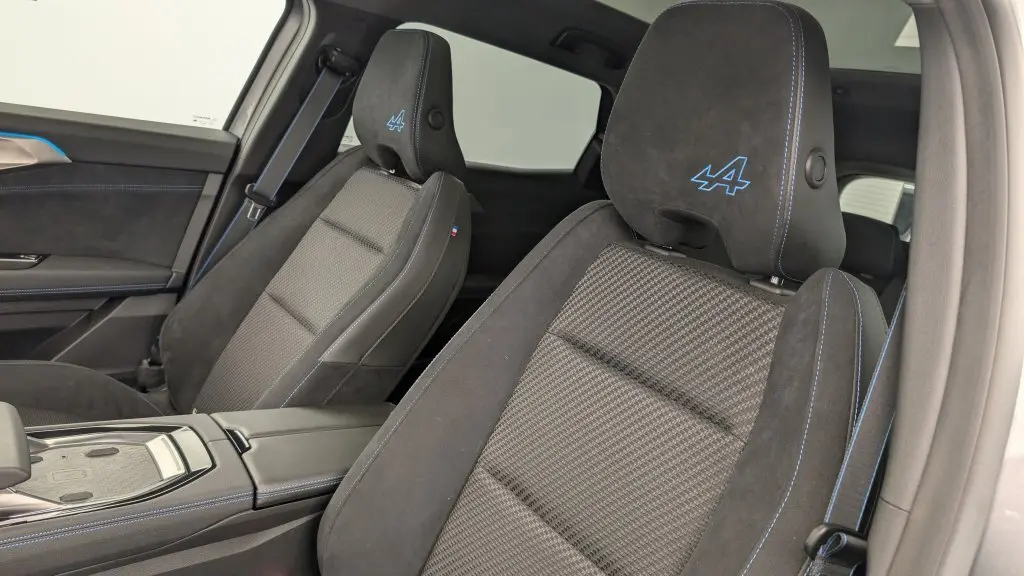 Gros plan sur les sièges avant en tissu carbone et alcantara gris avec surpiqûres bleues et logo Alpine brodé sur appuie-tête.