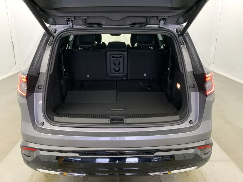 Coffre ouvert vu de l'arrière d'un Renault Espace gris schiste avec banquette arrière rabattue et feux arrière allumés.