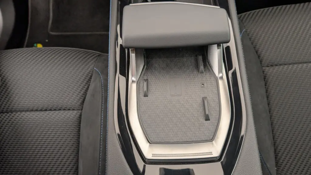 Gros plan sur le chargeur à induction central entouré de la sellerie mixte tissu carbone et alcantara avec surpiqûres bleues du Renault Espace gris Schiste.