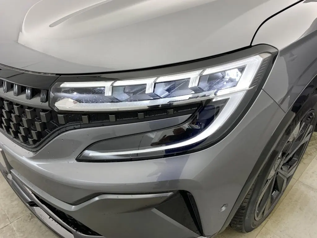 Gros plan sur le phare avant droit et la calandre à damiers du Renault Espace E-Tech gris schiste finition Esprit Alpine.