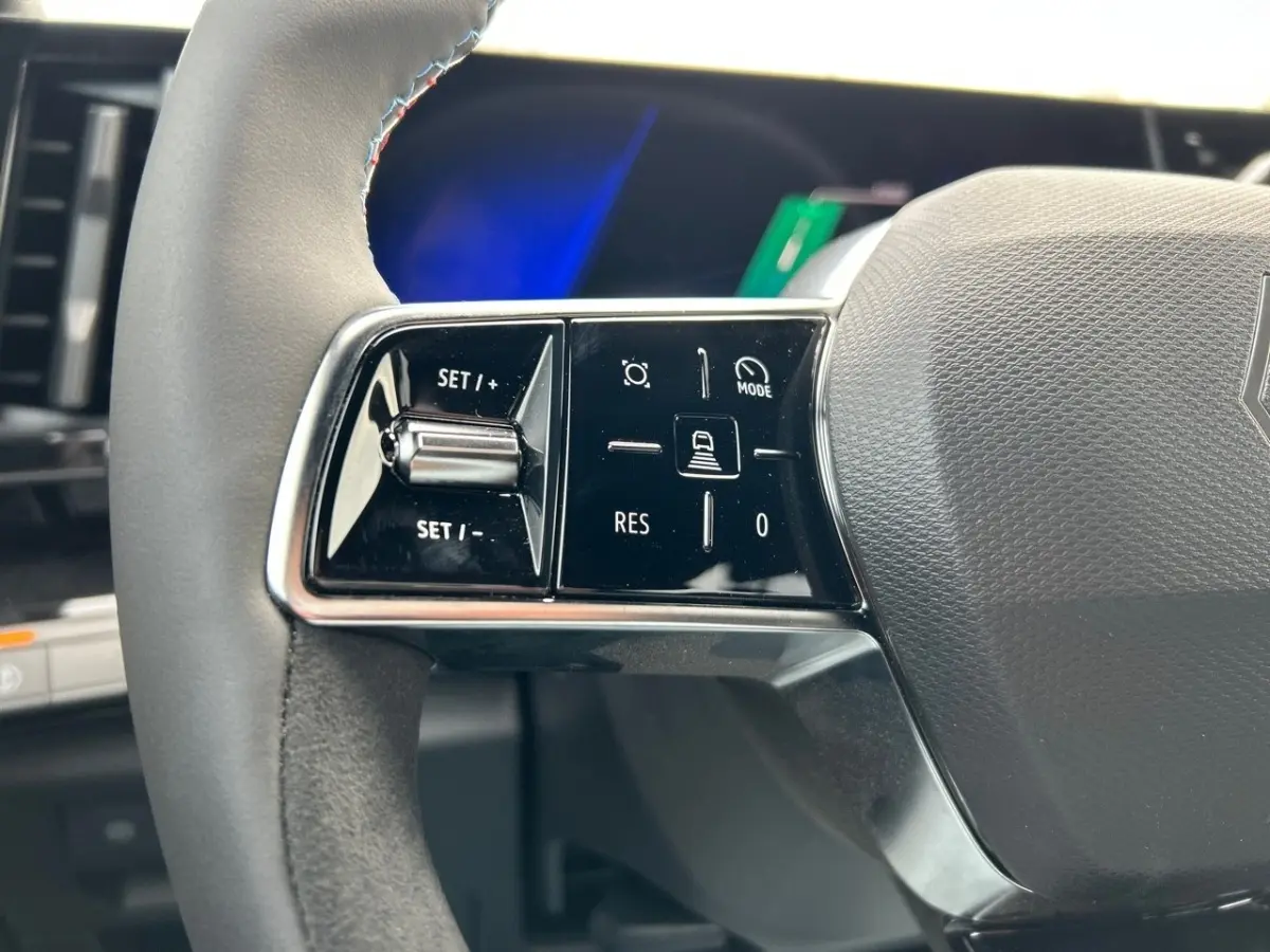 Gros plan sur les commandes gauche du volant noir du Renault Rafale esprit Alpine hybride 2025, avec boutons multifonctions.