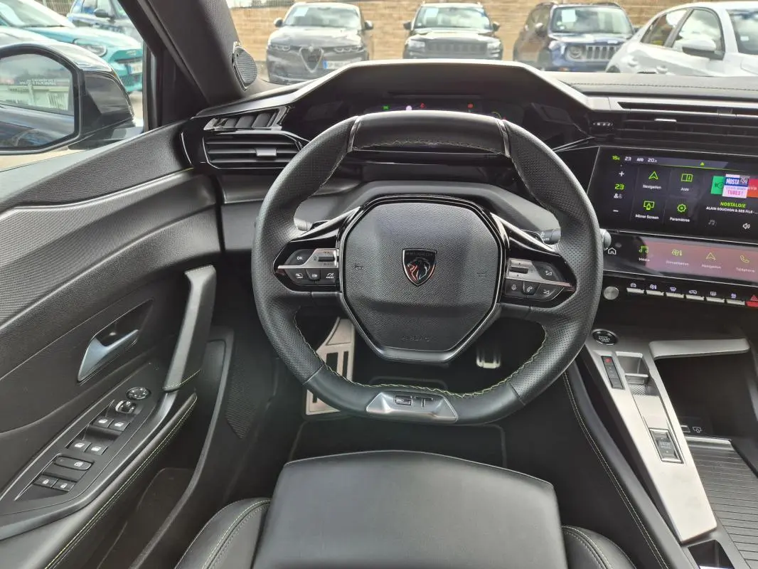 Vue intérieure frontale du volant cuir noir avec logo Peugeot et cockpit numérique lumineux du 408 Hybrid 2024.