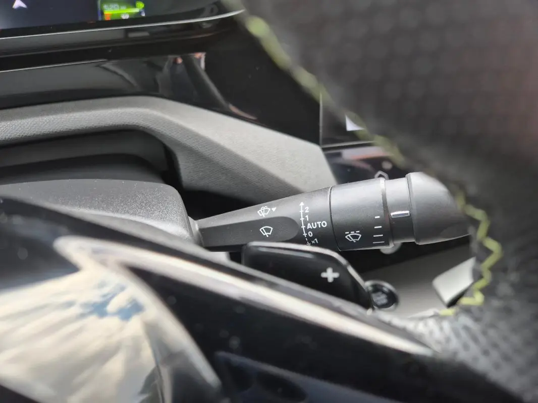 Gros plan sur la commande d’essuie-glace à gauche du volant cuir noir du Peugeot 408 Hybrid 2024.