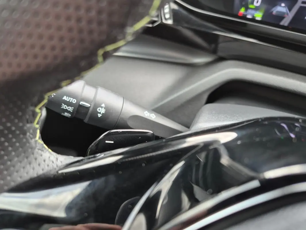 Gros plan sur le volant cuir et la commande des feux d’un Peugeot 408 Hybrid 136 e-DCS6 GT noir, intérieur moderne.