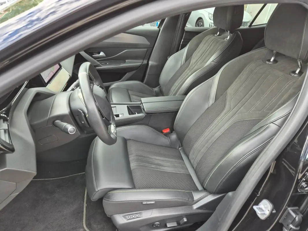 Vue intérieure côté conducteur de la Peugeot 408 Hybrid GT 2024 noire, sièges cuir et alcantara avec accoudoir central.