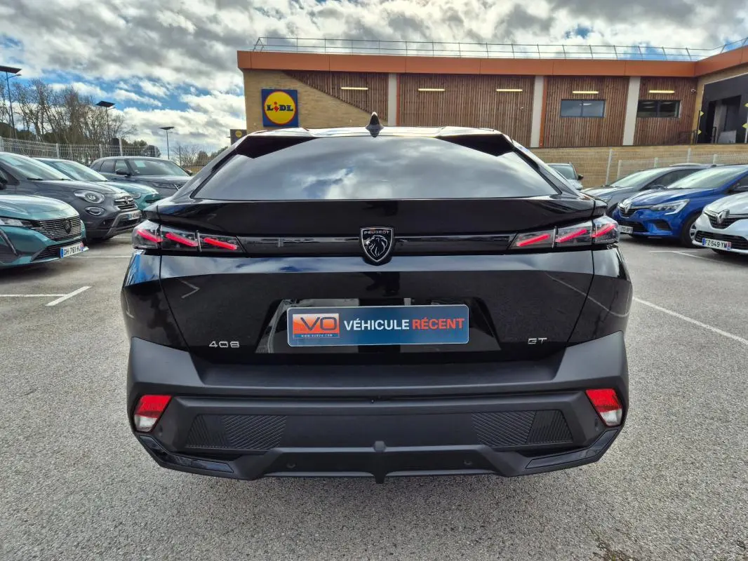 Vue arrière d'une Peugeot 408 noire 2024 avec feux LED distinctifs et logo lion central sur parking extérieur.