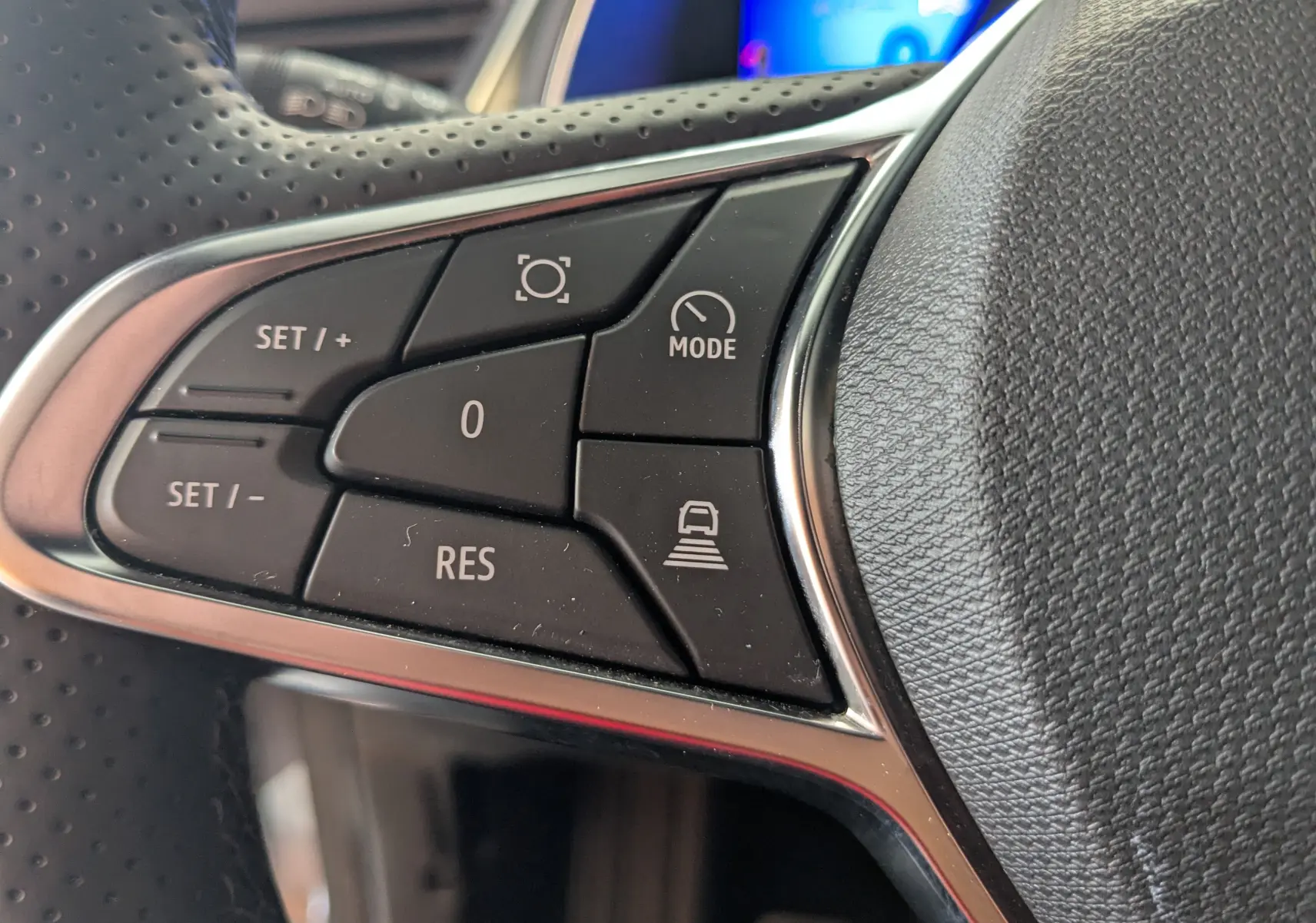 Gros plan sur les commandes noires du volant perforé de la Renault Symbioz gris Cassiopée, avec boutons de régulateur et mode.