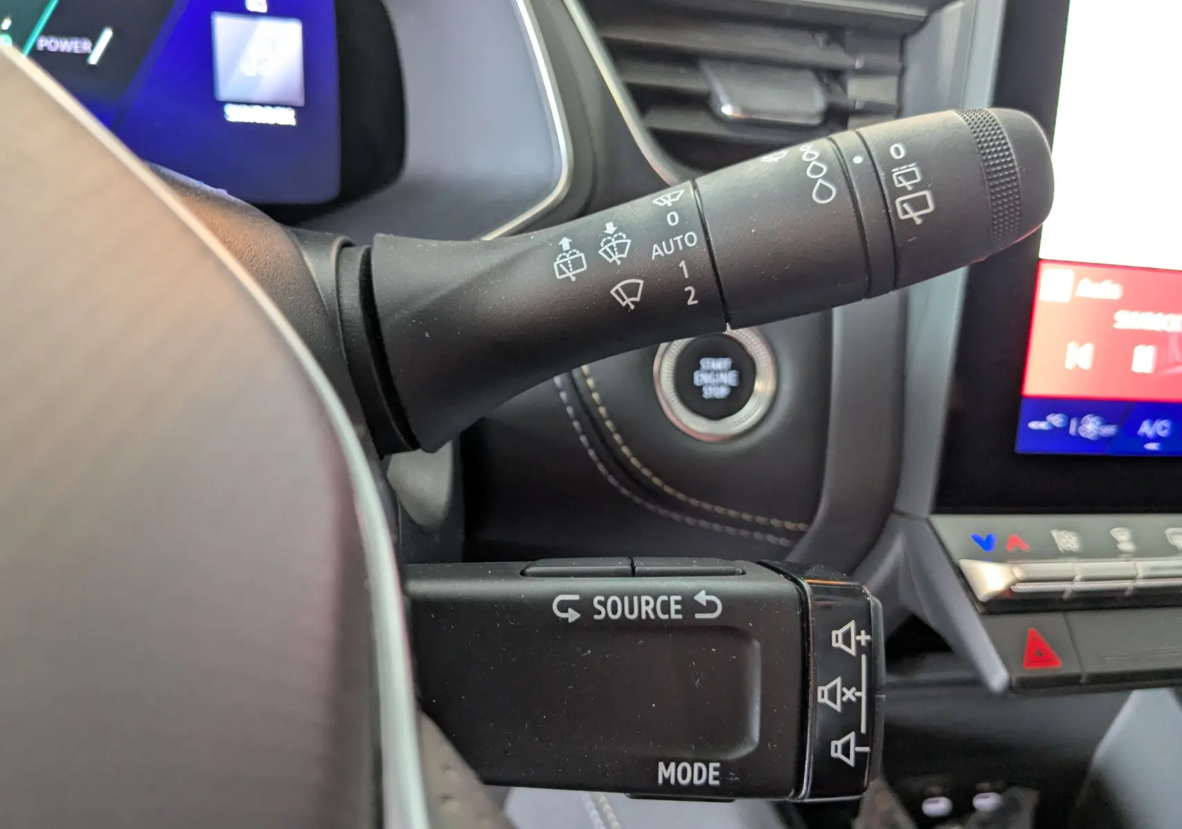 Gros plan intérieur sur les commandes au volant du Renault Symbioz gris cassiopée, avec affichage digital et bouton start/stop visible.