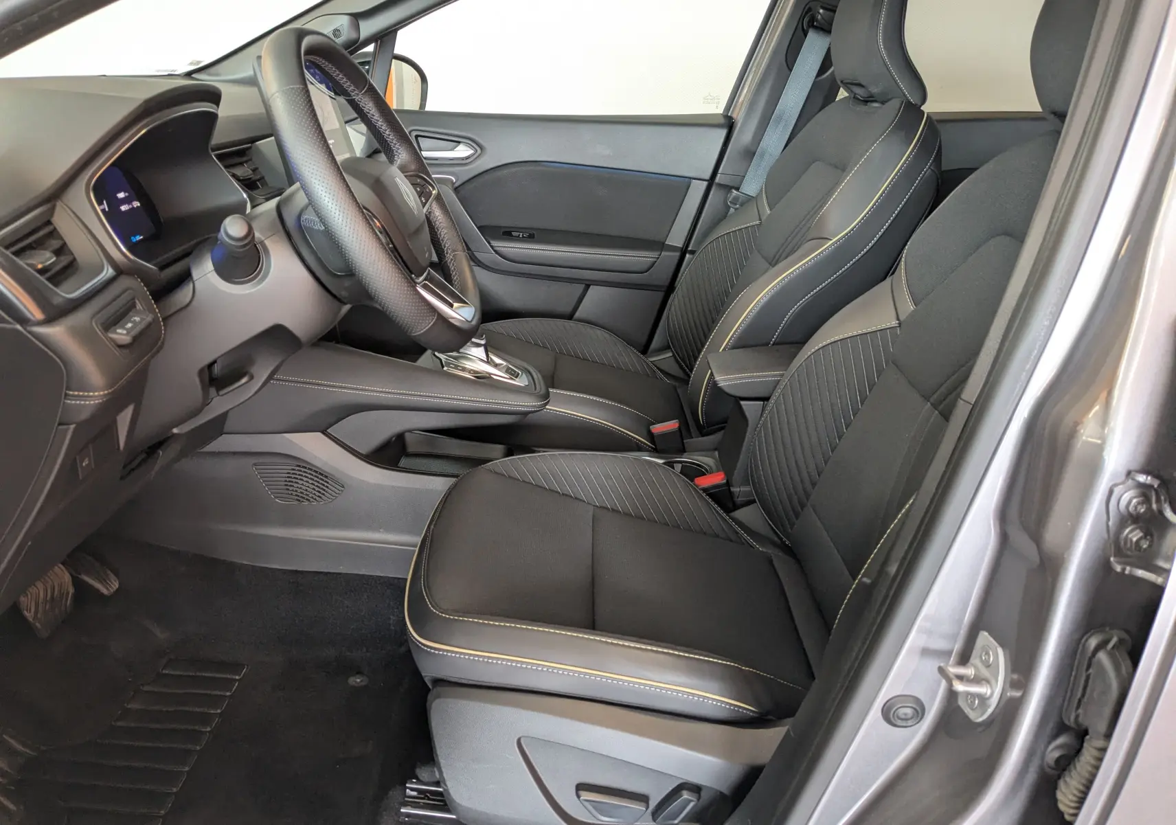 Vue intérieure côté conducteur de la Renault Symbioz E-Tech Full Hybrid 145 Iconic avec sièges noirs et surpiqûres jaunes.