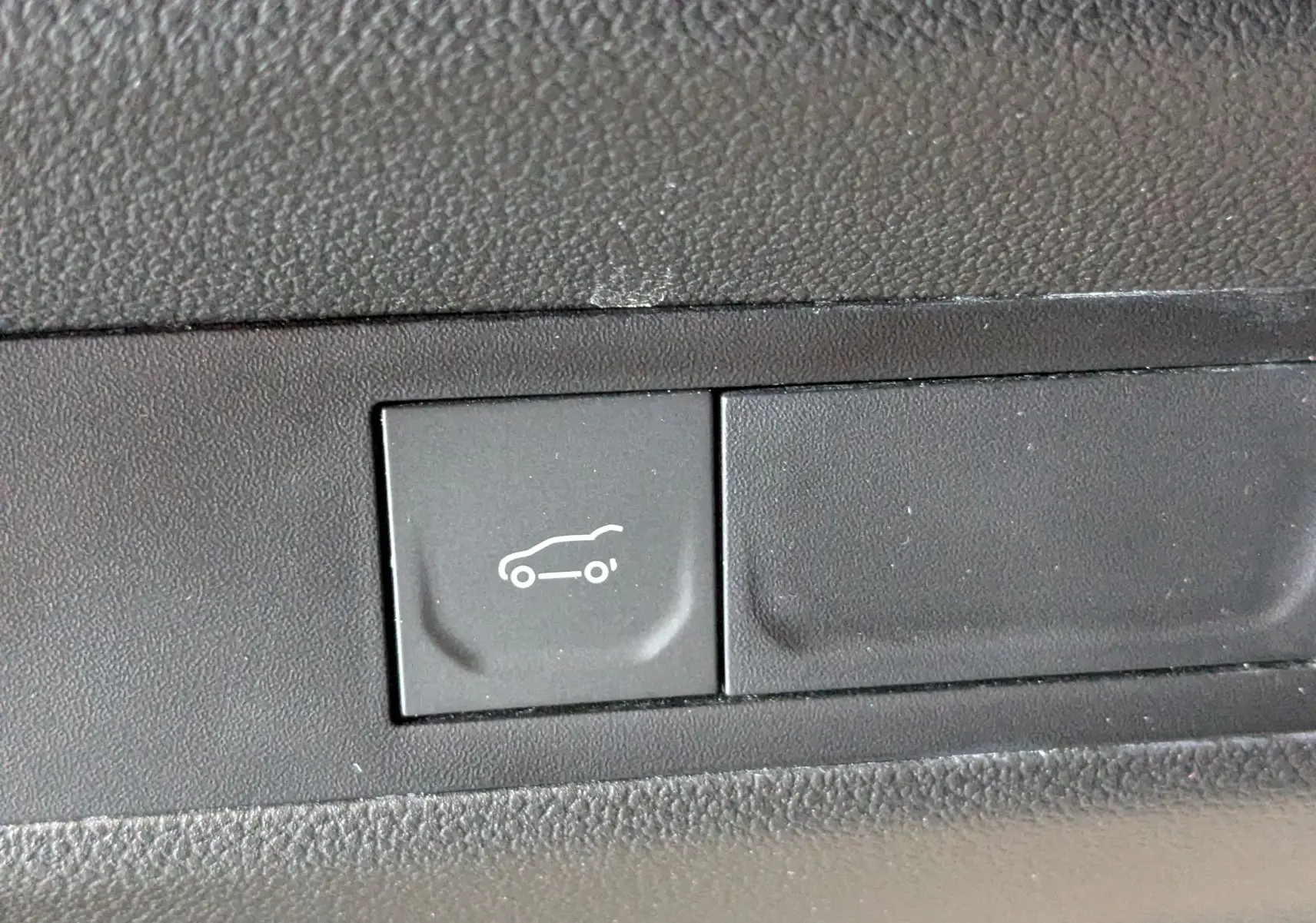 Bouton noir intérieur avec pictogramme blanc d'ouverture du coffre sur Renault Symbioz E-Tech gris Cassiopée.