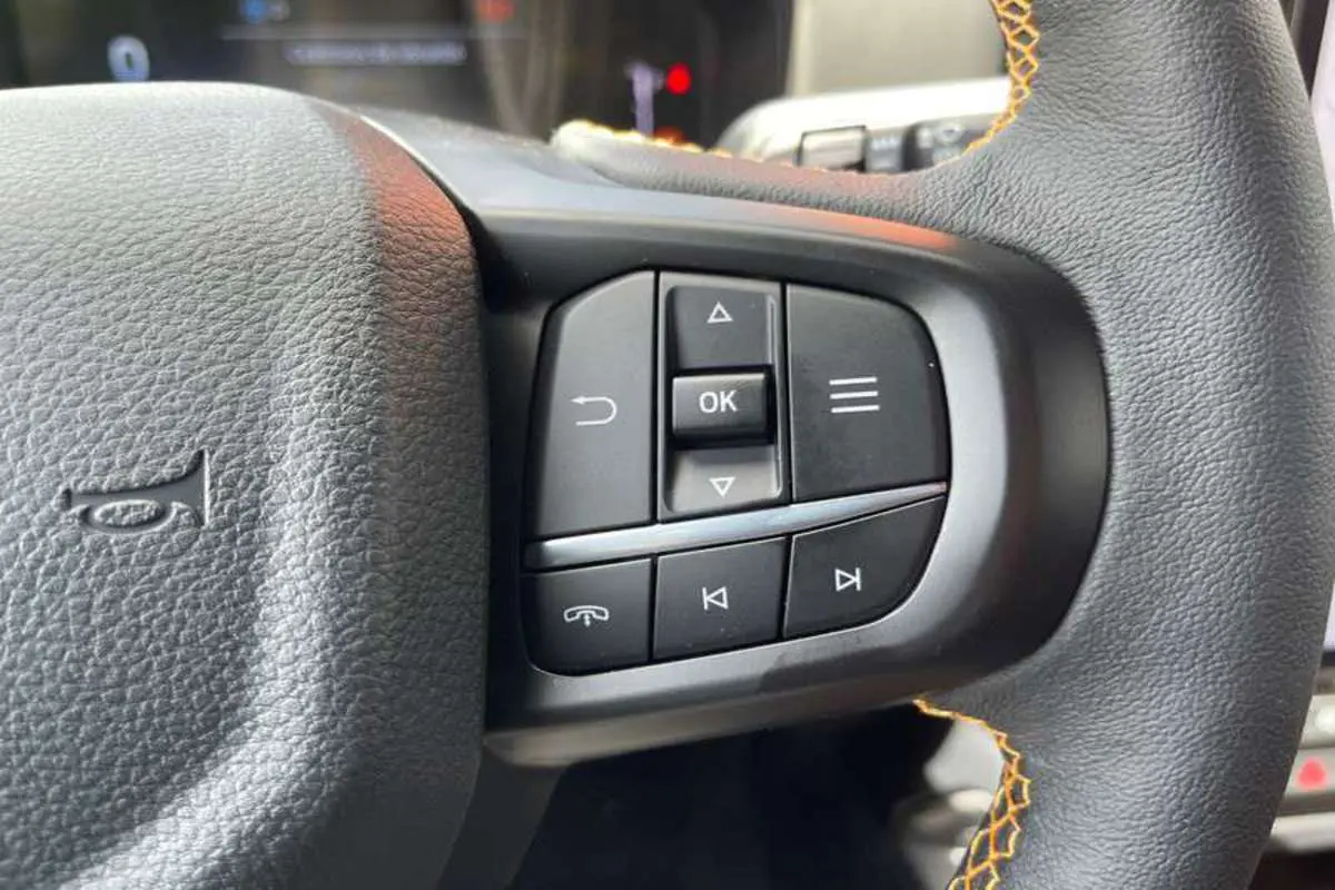 Gros plan sur les commandes multifonctions à droite du volant cuir noir avec surpiqûres orange du Ford Ranger Wildtrak 2025.