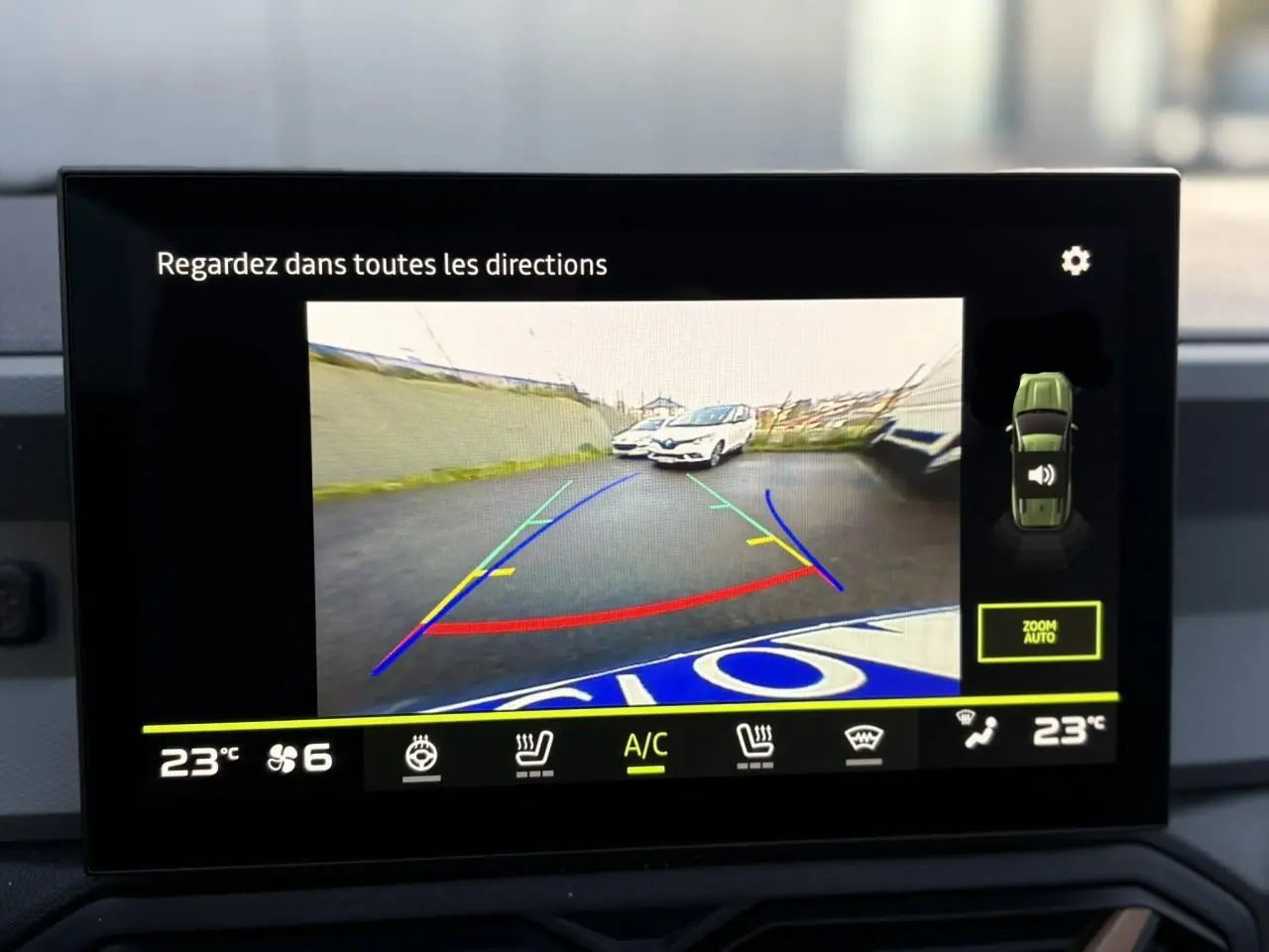 Écran de caméra de recul montrant l'arrière du Dacia Bigster noir nacré avec lignes de guidage colorées.