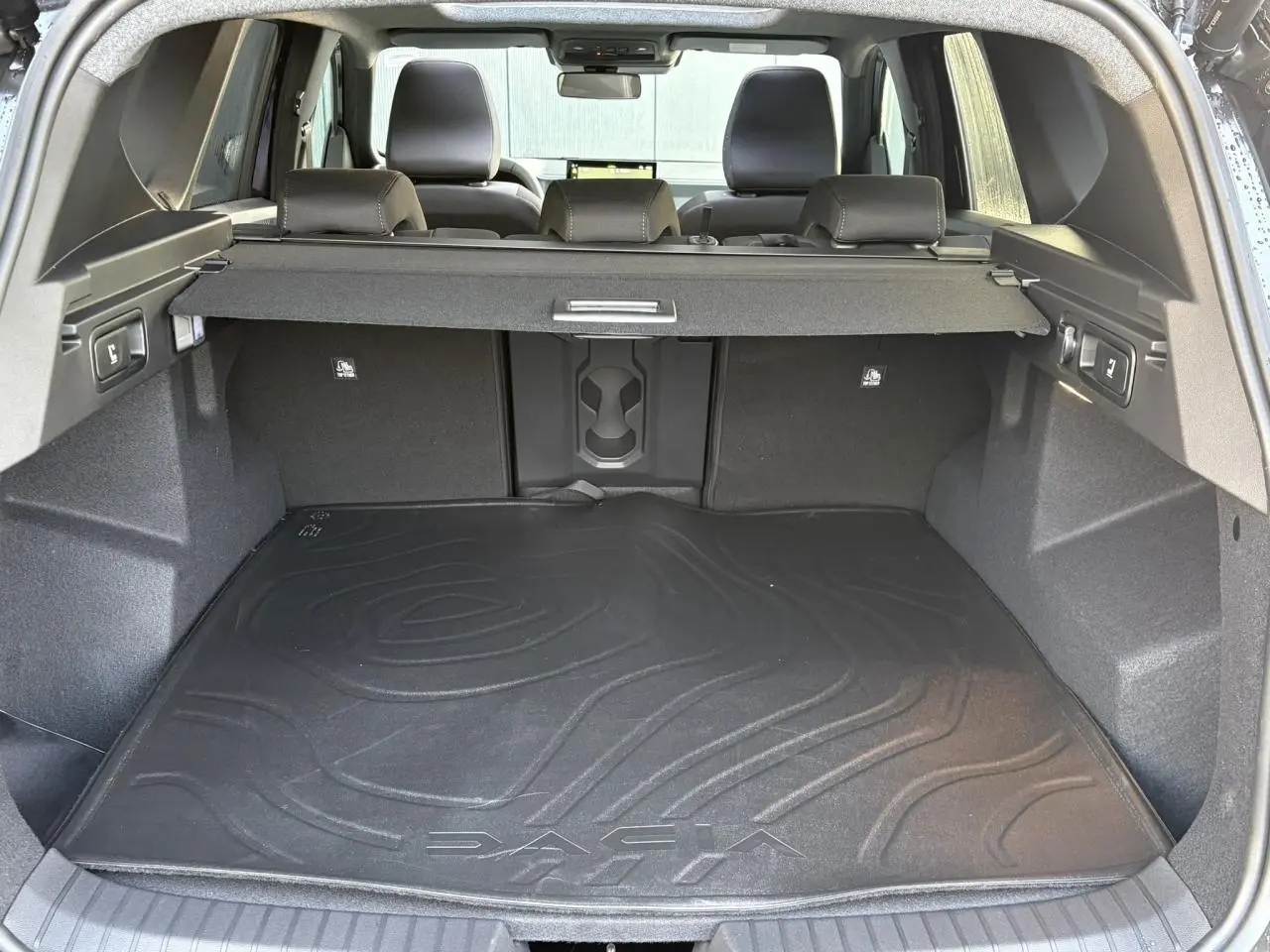 Vue depuis le hayon ouvert sur le coffre spacieux du Dacia Bigster 2026 avec tapis de sol noir et banquette arrière rabattable.