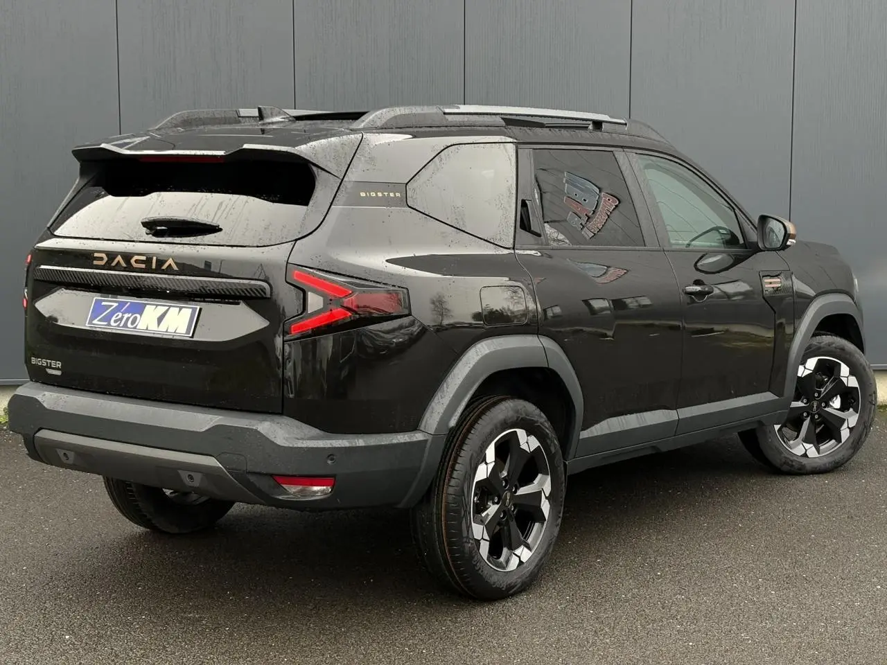 Vue 3/4 arrière droite du Dacia Bigster noir nacré avec jantes alliage et hayon électrique visible.