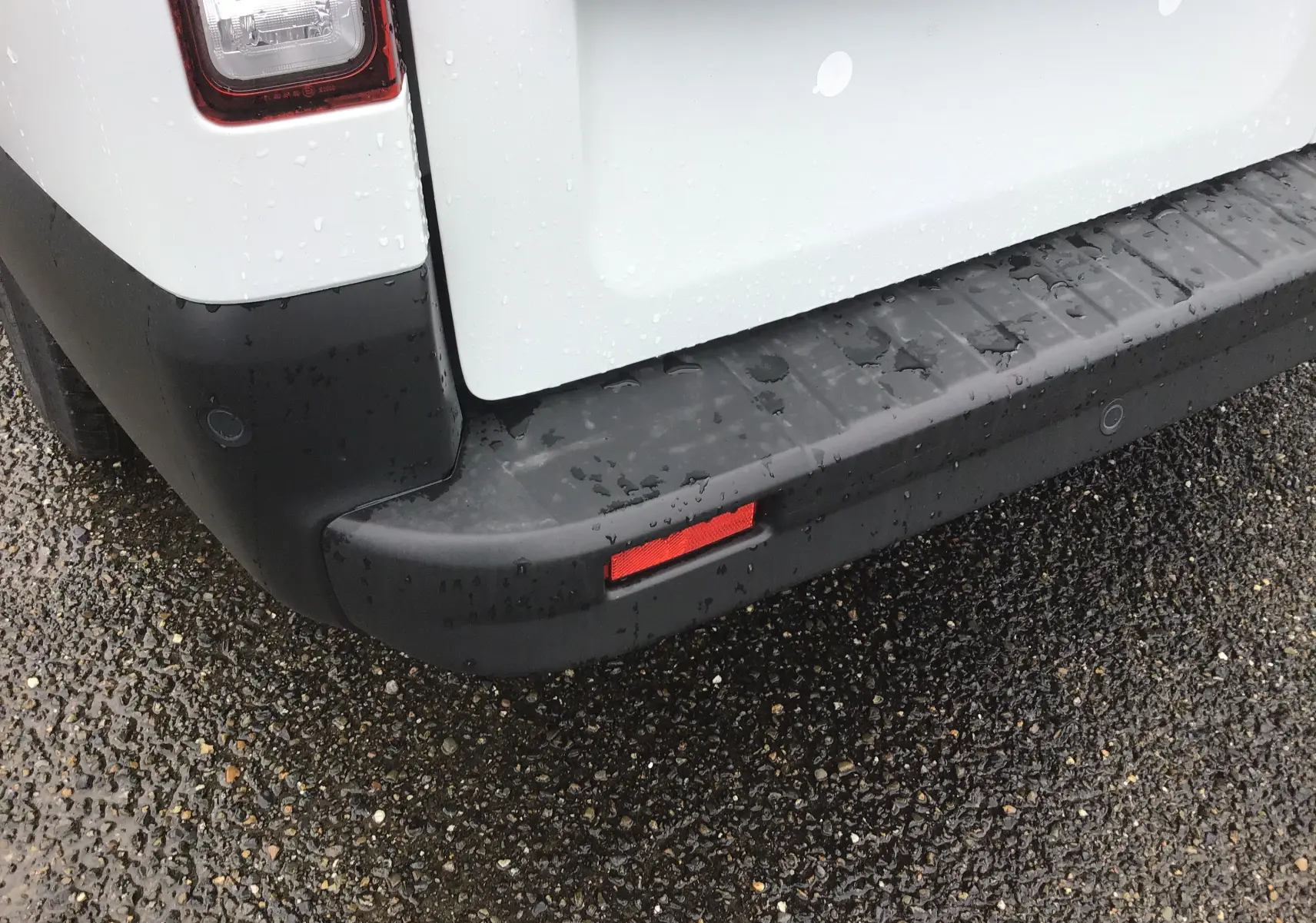 Gros plan sur le pare-chocs arrière noir et la partie blanche de la porte du Renault Trafic Fourgon L2H1 2023 sous la pluie.