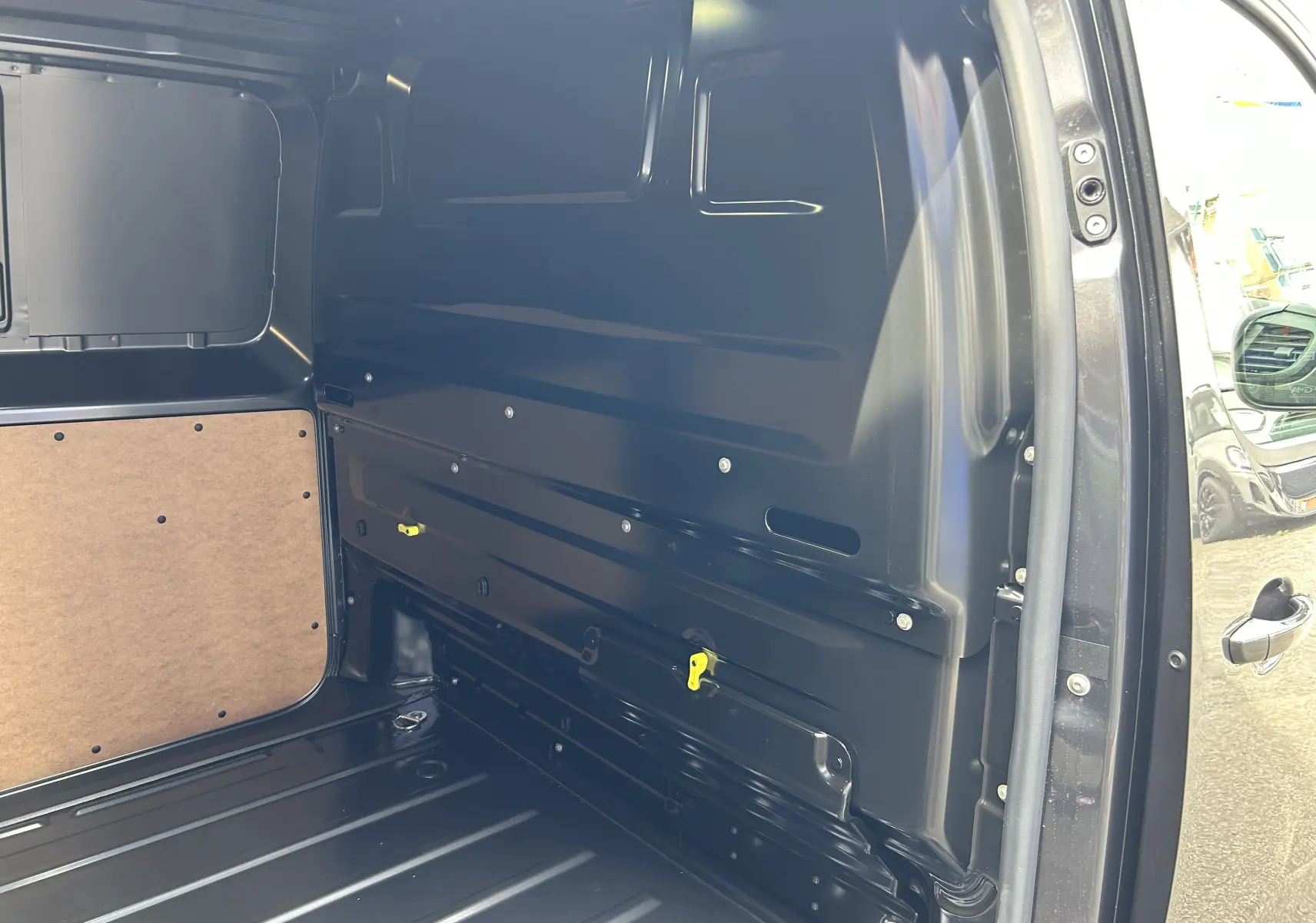 Vue intérieure côté droit du fourgon Citroën Jumpy gris acier, montrant la paroi métallique et un panneau en bois.