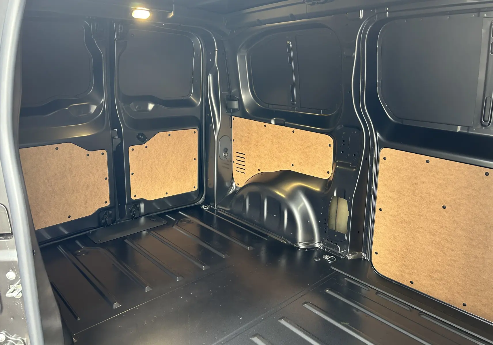 Intérieur du fourgon Citroën Jumpy Ph.2 gris acier, vue de l'espace de chargement avec panneaux bois sur parois métalliques noires.