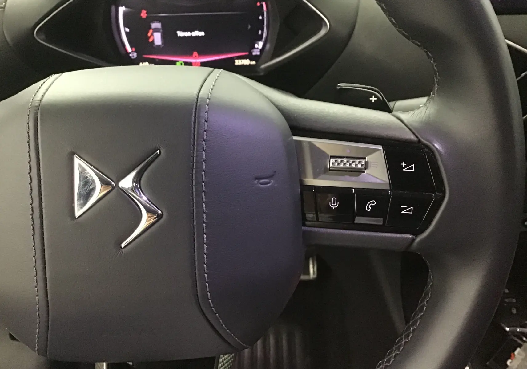 Gros plan sur le volant en cuir noir du DS3 Crossback 2024 avec commandes intégrées et logo DS chromé.