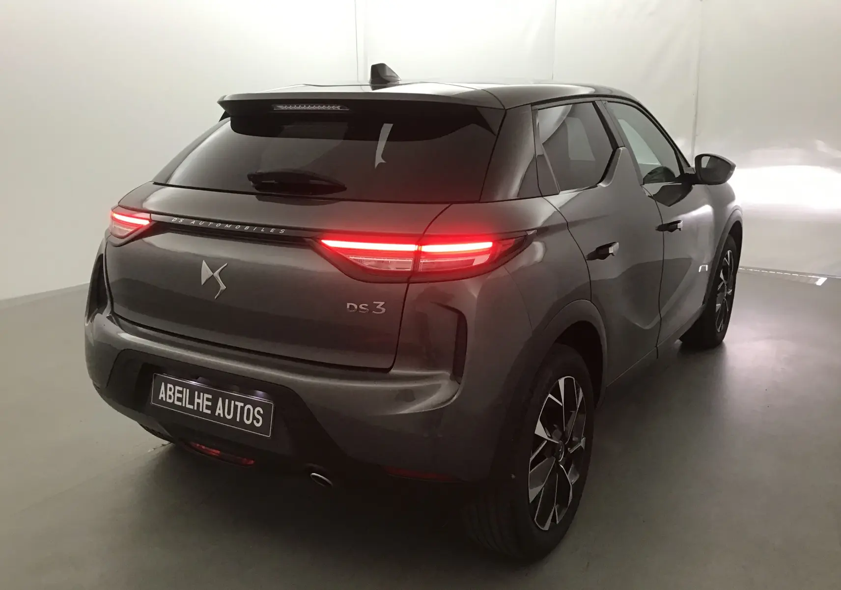 Vue 3/4 arrière droite d'un DS3 Crossback gris platinium 2024 avec feux arrière allumés dans un studio blanc.