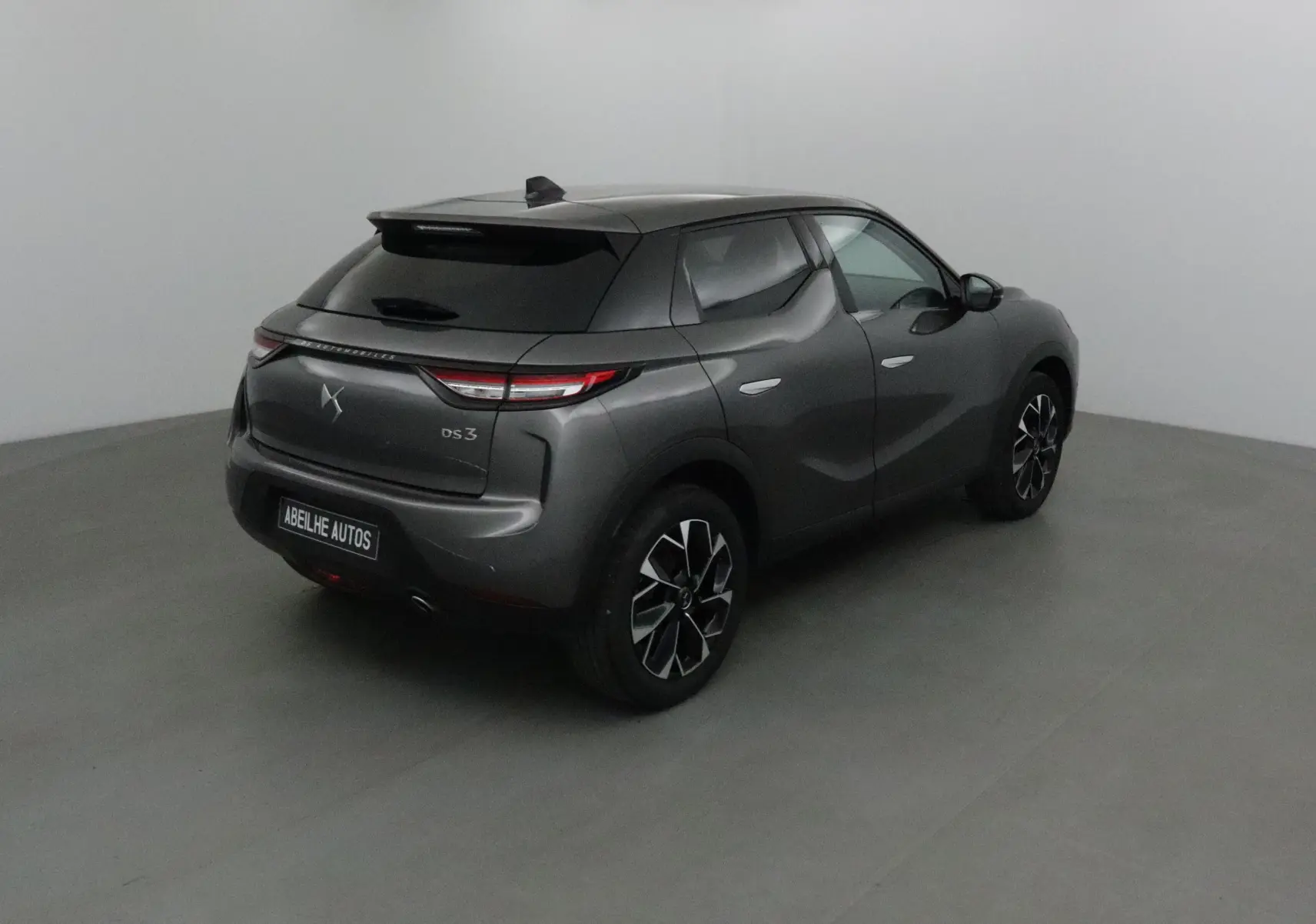 Vue 3/4 arrière droite d'un DS3 Crossback gris platinium avec jantes noires et feux arrière fins allumés.