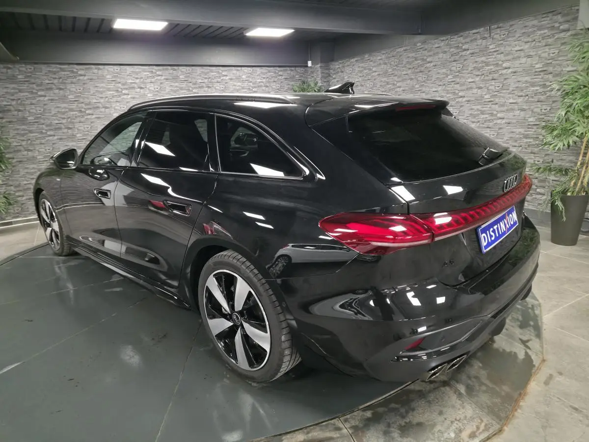 Audi A5 Avant noir vue 3/4 arrière droit en intérieur avec jantes 19 pouces et feux arrière LED continus.
