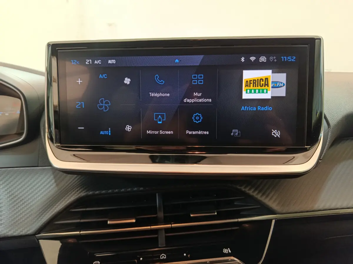 Écran tactile central de la Peugeot 208 gris clair 2025 affichant les options de climatisation et radio.