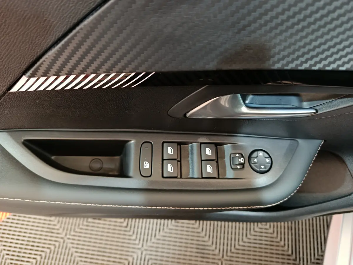 Gros plan sur la commande des vitres et rétroviseurs côté gauche de la porte intérieure noire de la Peugeot 208 gris clair 2025.