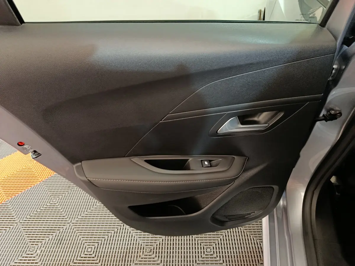 Vue rapprochée de la porte avant gauche gris clair de la Peugeot 208 PureTech 100 S&S Allure avec commandes de vitre et haut-parleur intégré.