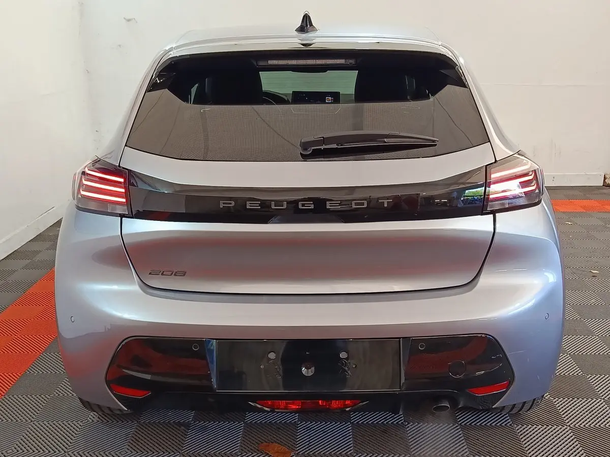 Vue arrière d'une Peugeot 208 gris clair 2025 avec feux LED et logo Peugeot lumineux sur hayon.