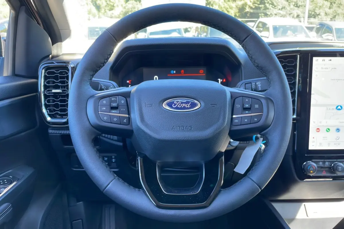 Vue rapprochée du volant cuir multifonctions noir du Ford Ranger 2025 avec tableau de bord numérique et écran tactile GPS.
