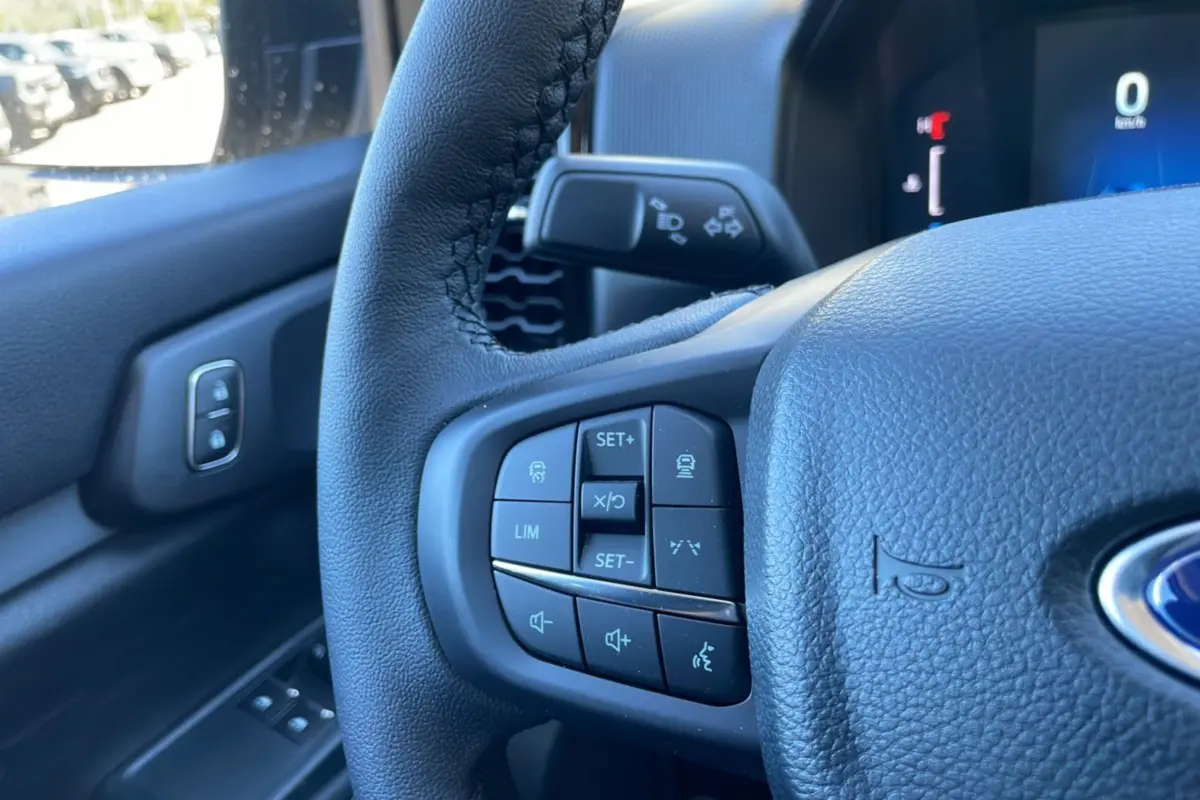 Gros plan sur le volant cuir noir du Ford Ranger 2025, avec commandes multifonctions et tableau de bord numérique en arrière-plan.